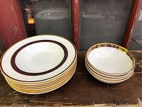 Two stacks of bowls side by side on wooden surface, one stack of shallow rimmed bowls and one of deeper cereal bowls.