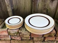 Two stacks of six plates each (small and large) on brick background.