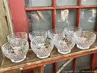 Eight clear crystal bowls with honeycomb facetted Boston pattern, arranged in two rows on a wooden surface in front of a red window frame.