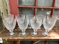 Nine Villeroy and Boch Boston pattern crystal glasses displayed in two rows on a wooden table in front of a red window frame, all showing clear honeycomb textured facets.