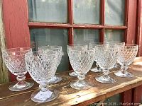 Nine Villeroy and Boch Boston crystal stemware glasses arranged in a row on a wooden ledge with a window background.