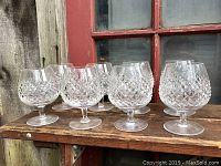 Eight brandy snifters arranged in two rows on a wooden ledge in front of a window.