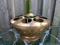 Overall front view of the brass bucket on table showing eight bottle openings around rim and central lid.