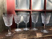 Front view of five Waterford crystal wine glasses in the Alana pattern displayed on a wooden surface with a window background.