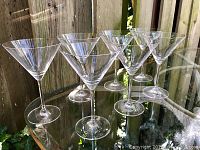 Eight vintage Waterford Marquis crystal martini glasses arranged in a cluster on a glass table outdoors, showing the shape and style of each glass from a side and slight top angle.