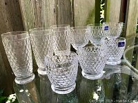 Nine clear crystal glasses with honeycomb facetted pattern displayed on mirrored surface outdoors. Includes six tall and three short glasses with thick bases and textured design. Two short glasses show Villeroy and Boch stickers.