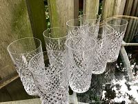 Eight facetted glasses arranged on a glass table against a wooden fence