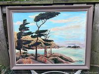 Full view of painting in frame depicting windswept trees on rocky shore and distant lake under blue sky