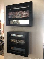 Front view of two small black-framed wall mirrors, one mounted above the other, showing abstract textured metal art and segmented mirror glass.