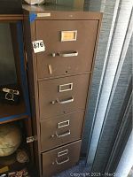 Brown metal file cabinet with four drawers visible, showing wear, scratches and dents on surface.