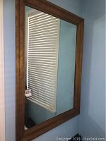 Full view of the rectangular wooden framed mirror hanging on a blue wall under natural light.
