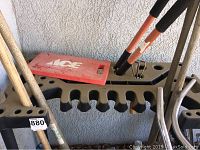 Photo of yard tool storage rack with several tools including shovels and rakes standing upright. Red Ace kneeling pad on top of rack.