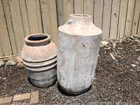 Two terra cotta outdoor pots of differing sizes photographed outside on soil with wooden fence background