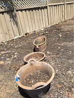 Three outdoor clay planters arranged on bare soil near a wooden fence, showing size variation and natural weathering.