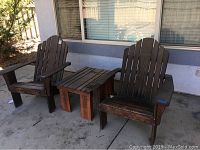 Two dark-stained wood Adirondack chairs alongside a matching wood square table on concrete ground outdoors; chairs and table show signs of wear and dirt from outdoor exposure.