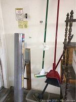Photo showing the cleaning supplies including push broom, broom, dustpan with brush, and the Pro Shield sheeting roll leaning against the wall