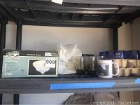 Shelf with boxed ceiling fixture, two clear or smoked glass cups, white ceramic mug, and multiple blue glass cups in molded packaging.