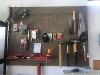 Pegboard mounted hand tools including saw, hammers, brushes, measuring level, and various small hand tools and accessories.