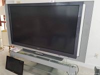 Sony Grand Wega 60-inch LCD TV on glass TV stand with small Samsung monitor beside it.