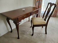 Full view of Queen Anne style desk and accompanying upholstered chair in room setting