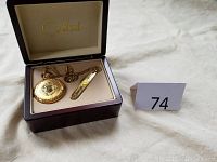 Open box showing gold pocket watch, knife, and chain arranged neatly inside with a lot number card beside it.