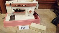 Side view of vintage pink and white Singer sewing machine with foot pedal on base.