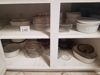 Wide view of lower and upper cabinet shelves showing glass and ceramic cookware including bowls, casserole dishes, and ramekins.