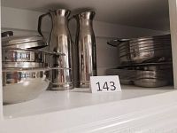 Photo showing stainless steel pitchers, plates, and bowls stacked on a shelf.
