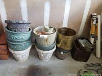 Full view of stacked assorted ceramic, brass, resin, and metal flower pots with various sizes and decorative styles.