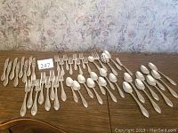 Overview of the full flatware set displayed on a wooden table, showing knives, forks, spoons, and serving utensils arranged neatly.