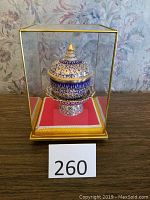 Full view of the blue and gold lidded dish within the glass case on a wooden surface, with item number 260.