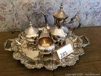 Silver tea service set including teapot, creamer, sugar bowl on a large ornate serving tray on wooden surface.
