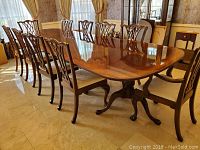 Full view of solid wood dining table with ten chairs arranged around it