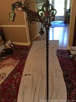 Full view of antique metal floor lamp standing on floor covering, showing twisted metal stand, lamp socket, and coiled cord
