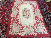 Full view of hooked wool rug with central floral medallion and red border.