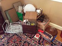 Wide view of all kitchenware items including boxes, racks, cake pans, thermos, food warmer, cheese board, and punch bowl on floor.