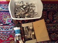 Overall photo of multiple flatware pieces in plastic and cardboard containers placed on patterned carpet.
