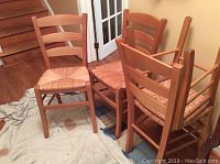 Four wooden Crate and Barrel rushed chairs grouped together, showing natural wood color, ladder backrests, and rushed seats.