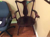 Full view of antique inlaid wooden armchair on hardwood floor, showing curved armrests and overall structure.