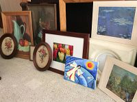 Nine framed pictures and two empty frames arranged on the floor, showing variety of artwork and frame styles