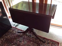 View of the closed wooden drop leaf table showing dark wood finish and rectangular top.