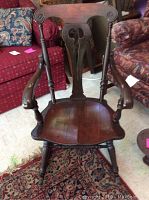 Front view of antique wooden rocking chair showcasing carved backrest, armrests, and contoured seat