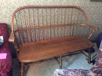 Full view of the maple wood bench showing curved spindle backrest and armrests, set against patterned wallpaper.
