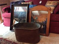 Photo showing copper vat in front of two wooden framed mirrors on carpet in front of couch.