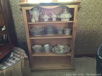 Full front view of the maple bookcase with four shelves filled with china dishes to show shelf spacing and size.