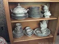Shelf showing stacked plates, bowls, cups, sugar bowl, creamer, covered serving bowl, and platters.