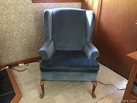 Front view of blue upholstered wingback chair with wooden cabriole legs showing seat, backrest, and armrests.