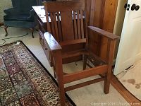 Full view of the antique wooden Morris style chair showing slatted backrest, armrests, and missing cushion.