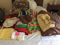 Overview of linens on bed, showing afghans, comforters, towels, napkins, and curtains folded