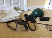 Full lot showing helmet, saddle blanket, gloves, crop, stirrups with strap, and grooming brush on carpeted floor.